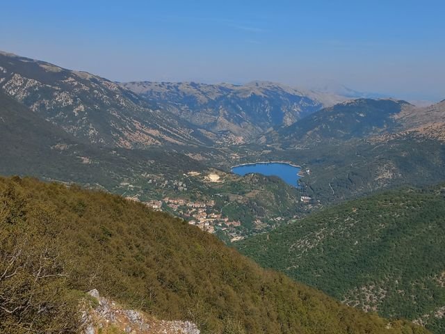 Il Lago di Scanno, di un blu intenso, e il paese sotto, visti dall'alto da un pendio di faggi con un bordo di roccia in primo piano