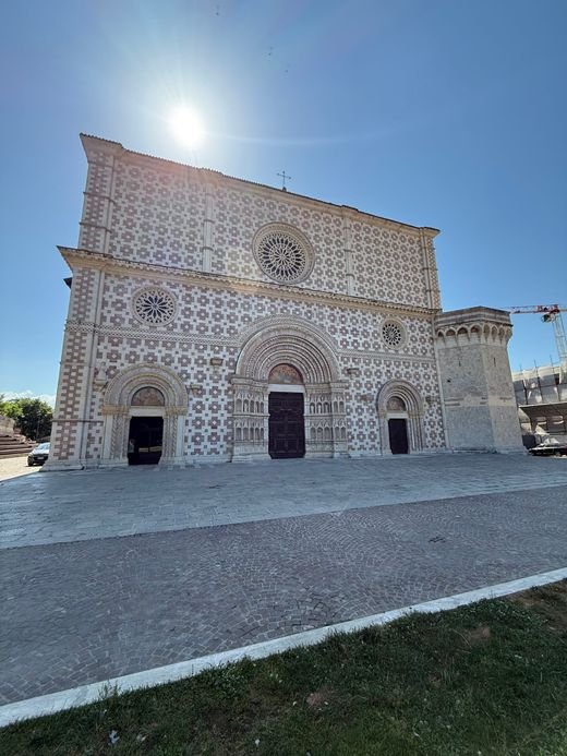 La facciata della Basilica di Collemaggio, a scacchi di pietra bianca e rosa, con il sole alto nel cielo sereno