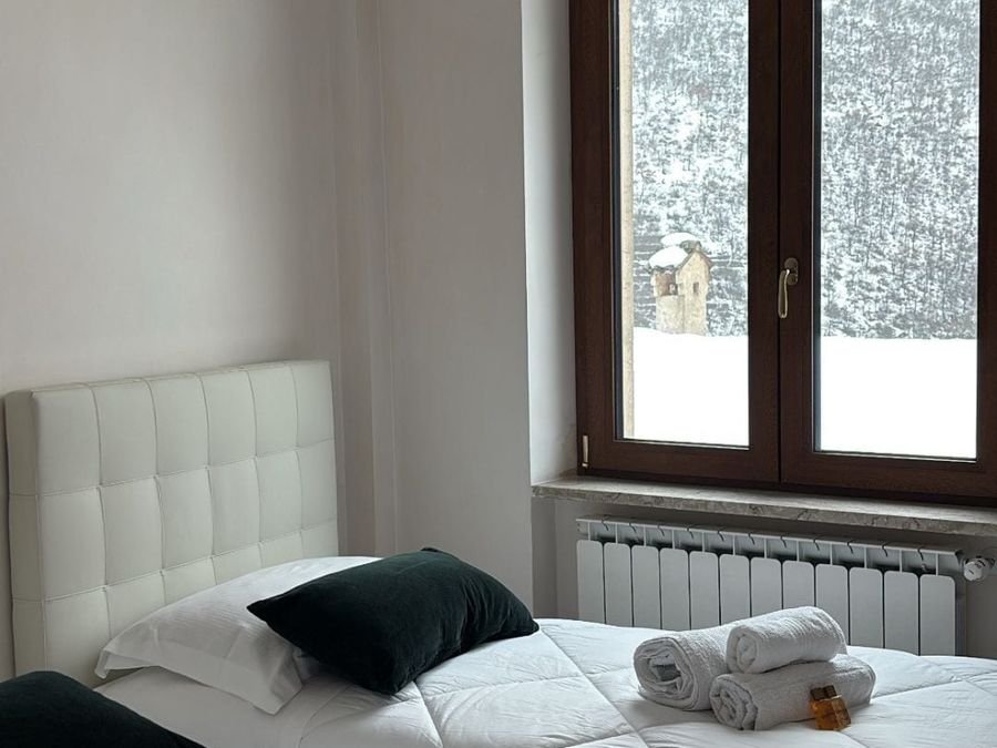 Bedroom with two single beds; outside the window, woods covered in snow