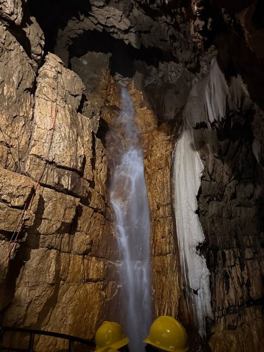 Una cascata dentro la grotta, tra rocce stratificate illuminate da luci calde