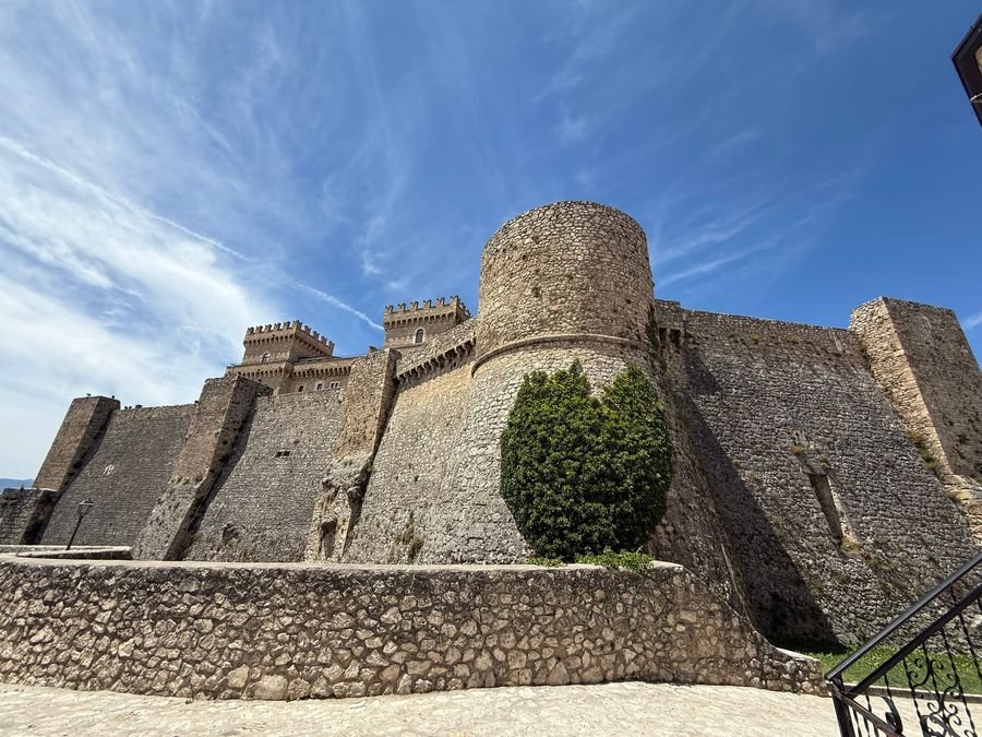 Il Castello Piccolomini di Celano: una torre rotonda e le mura di pietra, sotto un cielo azzurro con nuvole sottili