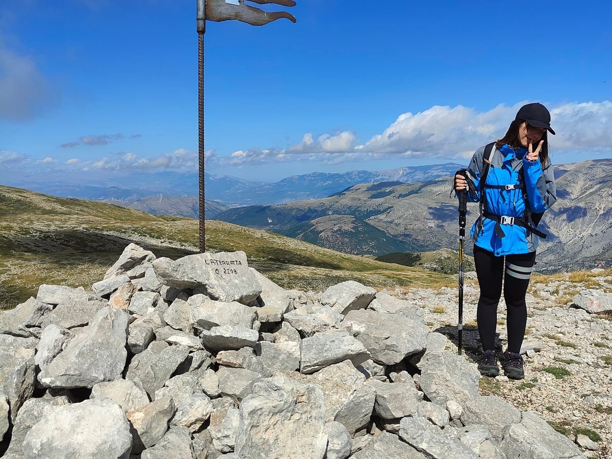 Un cumulo di sassi con la pietra incisa «La Terratta Q. 2208» e un'asta di ferro con una bandierina sagomata, sulla cima, con le montagne dietro