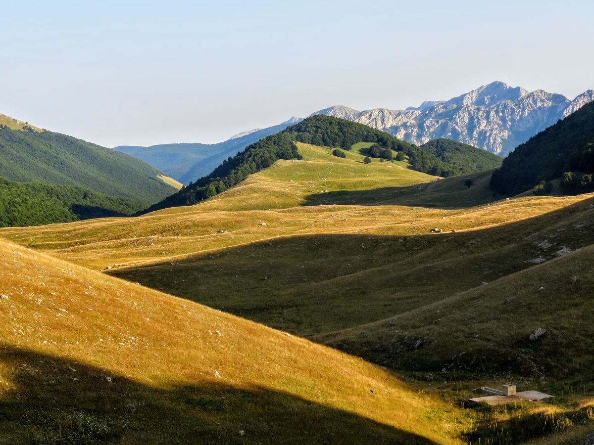 Colline di erba dorata e boschi di faggio nella Piana di Ferroio, con una montagna rocciosa sullo sfondo