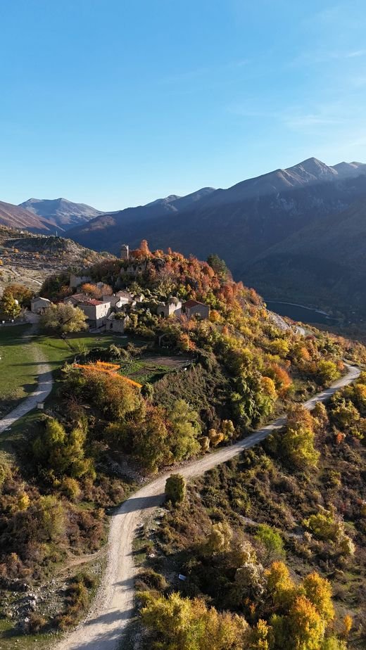 Frattura Vecchia vista dall'alto: case di pietra e ruderi su un'altura, tra alberi autunnali, con il lago e le montagne a destra