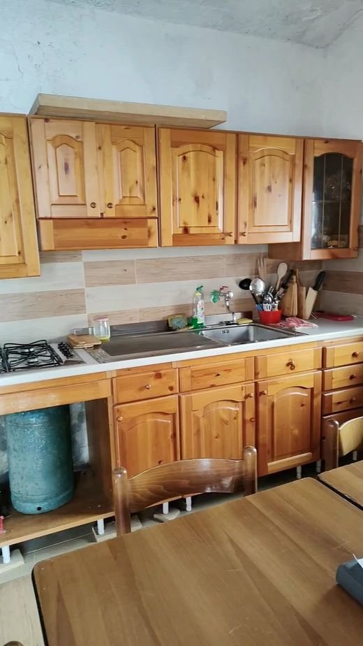 La cucina del rifugio: mobili di legno chiaro, lavello, fornelli a gas e una bombola, con il tavolo in primo piano