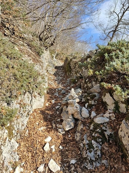 La Ruvella sul sentiero 26: un passaggio stretto tra due muri di roccia, con foglie secche sul fondo e un ometto di pietre