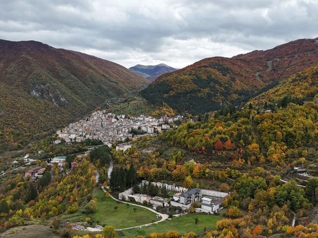 Scanno visto dal drone in autunno, con i boschi gialli e rossi intorno al paese e le montagne dietro