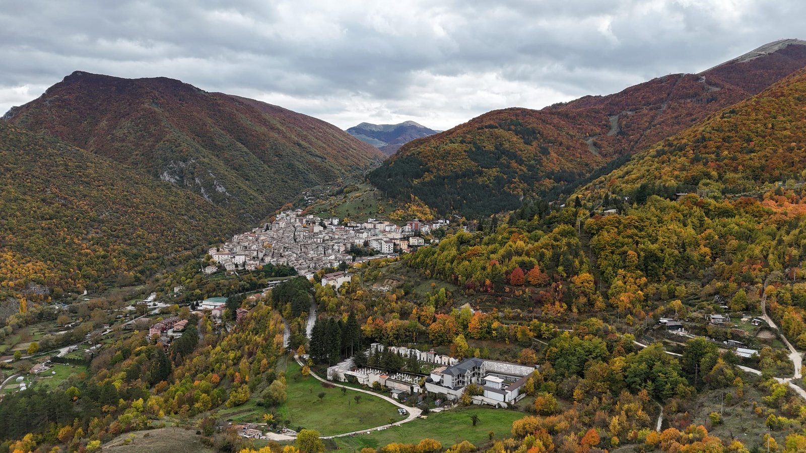 Scanno from a drone in autumn, with yellow and red woods around the village and mountains behind