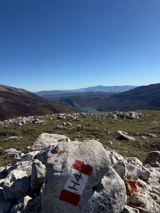 Il segnale bianco e rosso H4 dipinto su un sasso, con il Lago di Barrea in lontananza