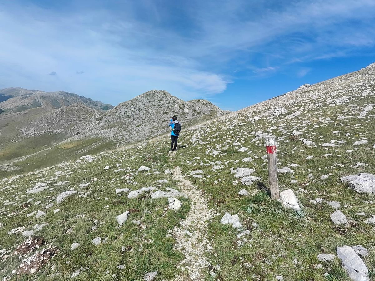 Un'escursionista sul sentiero A4, un filo di sassi bianchi, accanto a un paletto bianco e rosso del CAI