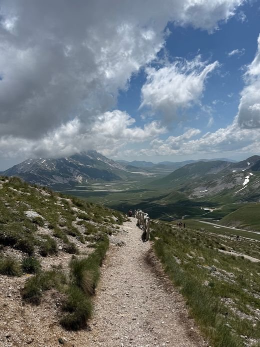 Il sentiero di ghiaia che sale lungo il crinale verso il Rifugio Duca degli Abruzzi, con la valle e le nuvole sullo sfondo