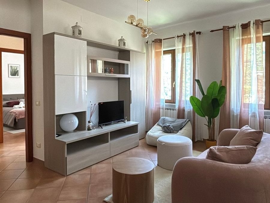 Living room with sofa, TV unit, pouf and two curtained windows