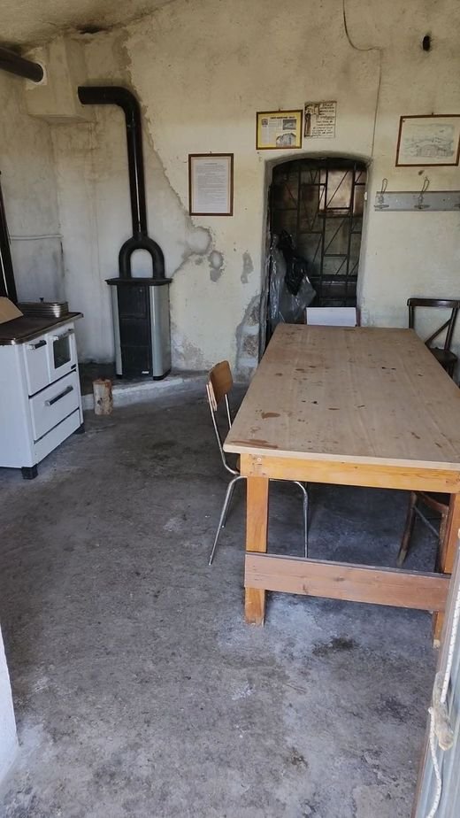 L'interno dello stazzo: un tavolo di legno lungo con le sedie, una stufa a legna e una cucina bianca contro il muro