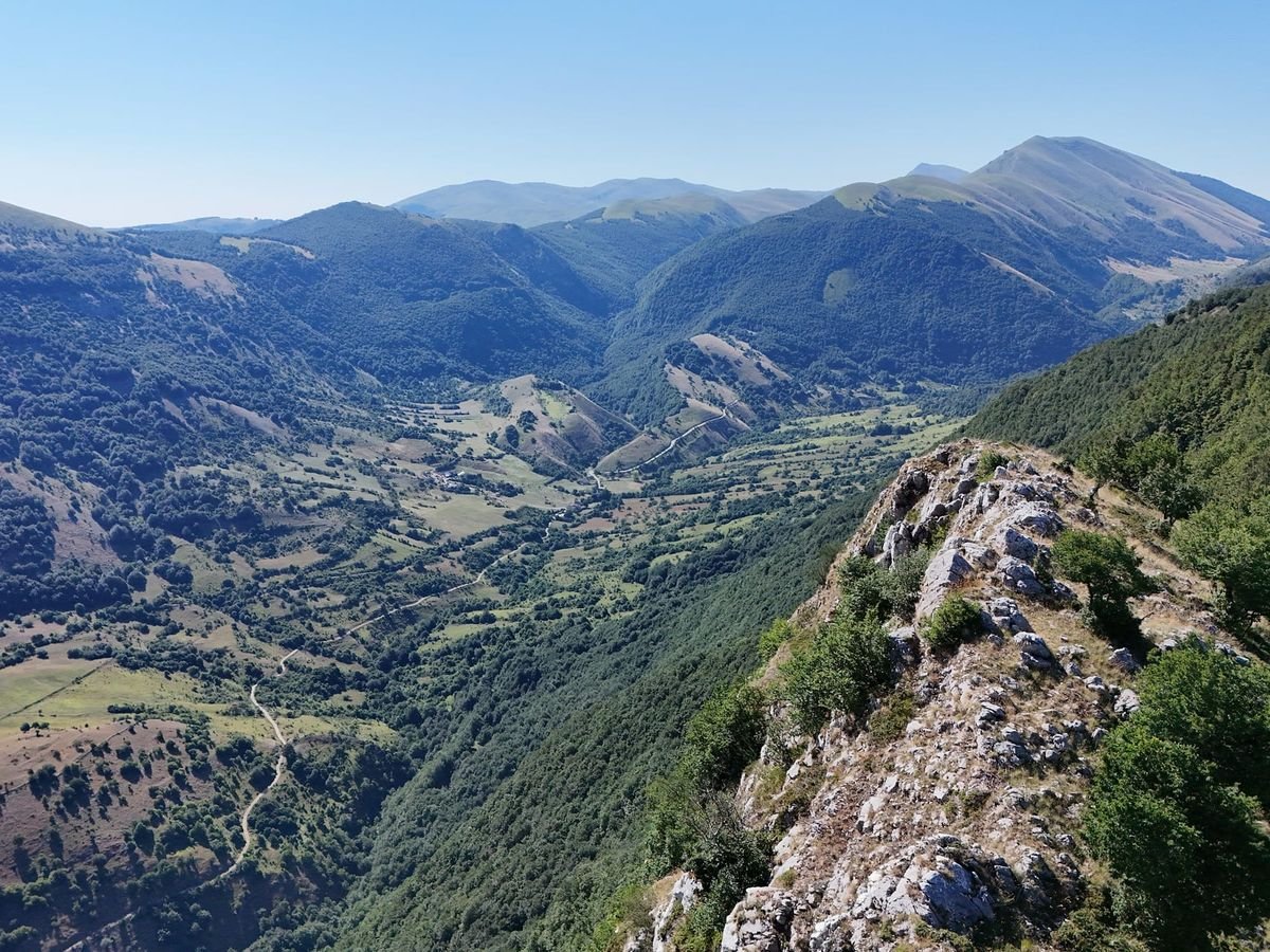 Dal Balzo della Mira: un costone di roccia e faggi in primo piano e, sotto, la valle di Jovana con le strade bianche tra i prati