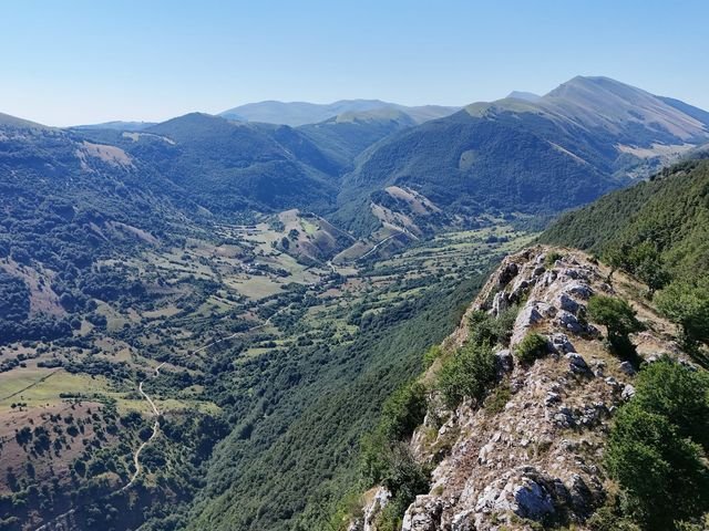 Dal Balzo della Mira: un costone di roccia e faggi in primo piano e, sotto, la valle di Jovana con le strade bianche tra i prati