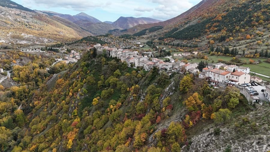 Villalago from a drone in autumn, with houses along the ridge and colourful woods below
