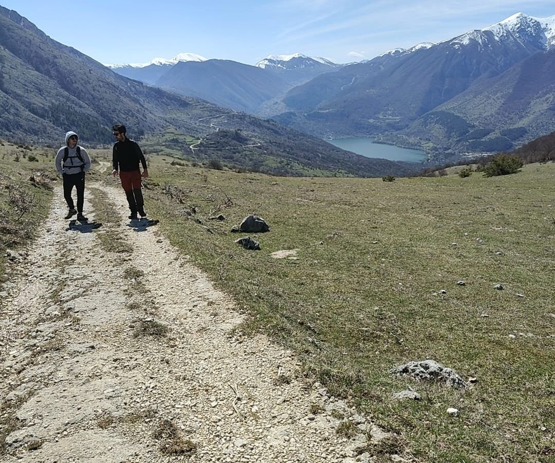 Due escursionisti su una strada bianca di sassi, con il Lago di Scanno e le montagne innevate in fondo alla valle