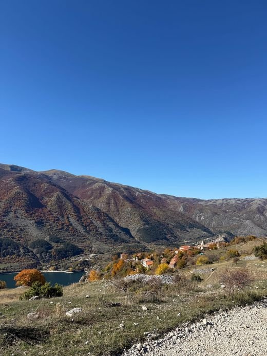 Il Lago di Scanno in basso a sinistra e Frattura, con i tetti rossi tra gli alberi d'autunno, davanti alle montagne boscose sotto un cielo blu