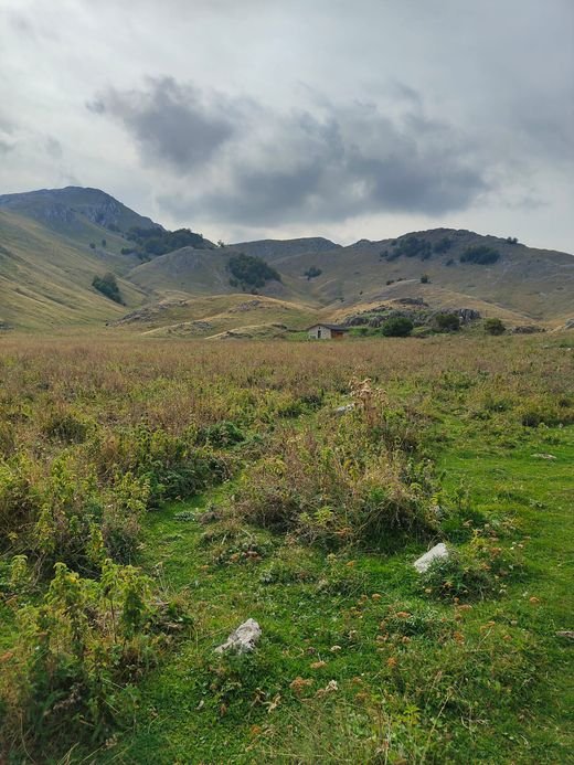 Lo Stazzo di Campo Rotondo, una casetta di pietra piccola in fondo a un prato, sotto montagne di erba e roccia